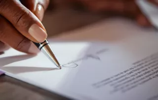Close-up of a hand holding a pen, ready to sign a document, symbolizing formal decisions in estate planning.