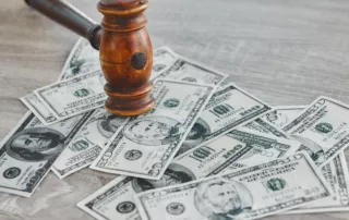 Wooden gavel resting on a pile of U.S. dollar bills on a wooden surface — symbolizing legal authority, debt, and financial-law decisions such as wage garnishment or bankruptcy.