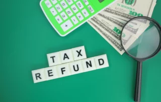 Calculator, magnifying glass, hundred‑dollar bills and Scrabble tiles spelling ‘TAX REFUND’ on green background, illustrating using a tax refund for Chapter 13 plan payments in New Jersey